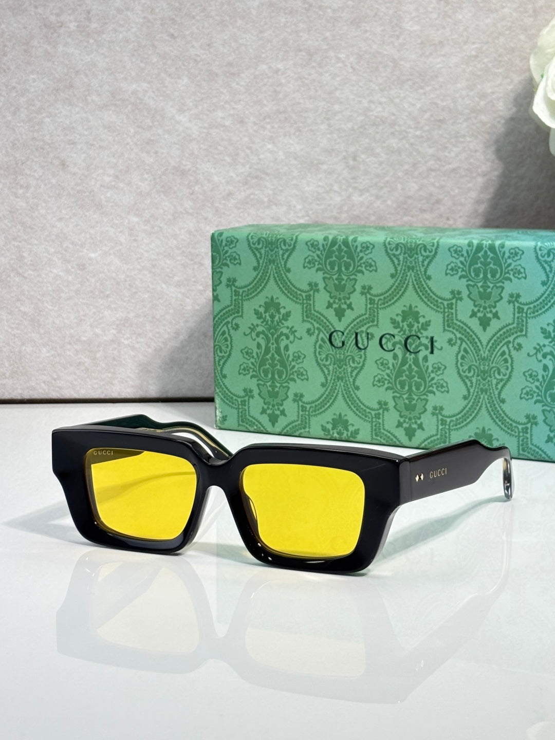 Black rectangular sunglasses with yellow lenses and Gucci logo on side arms.