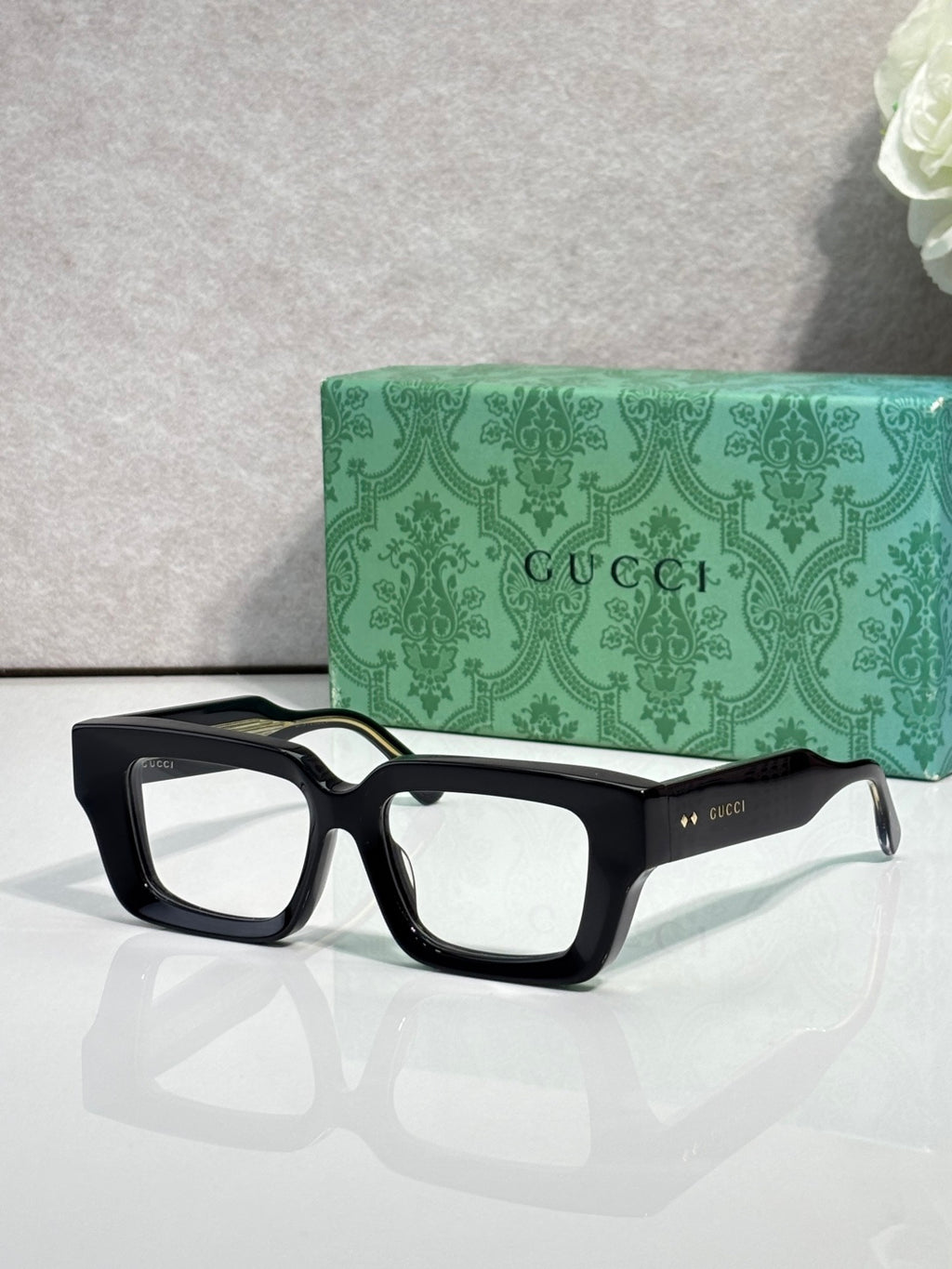 Black rectangular sunglasses with clear lenses and Gucci logo on side arms.