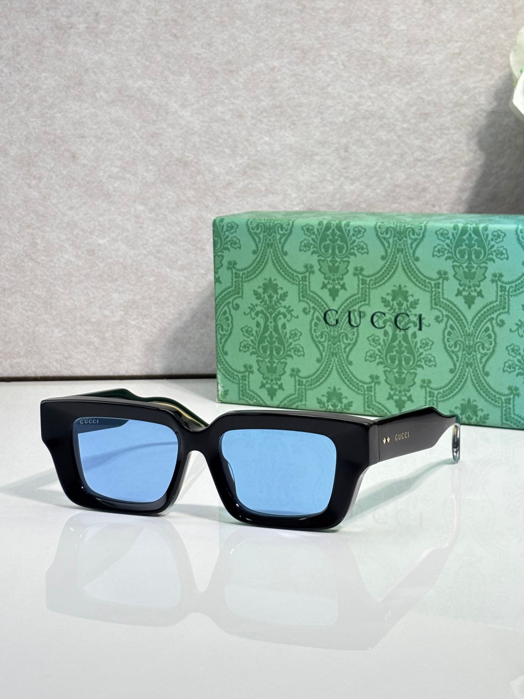 Black rectangular sunglasses with light blue lenses and Gucci logo on side arms.