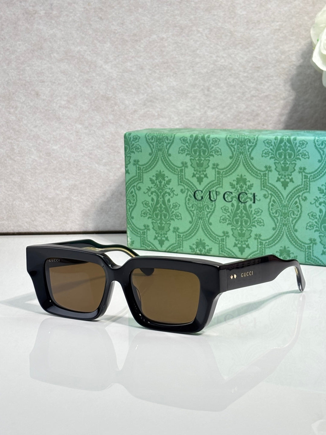 Black rectangular sunglasses with muted brown lenses and Gucci logo on side arms.