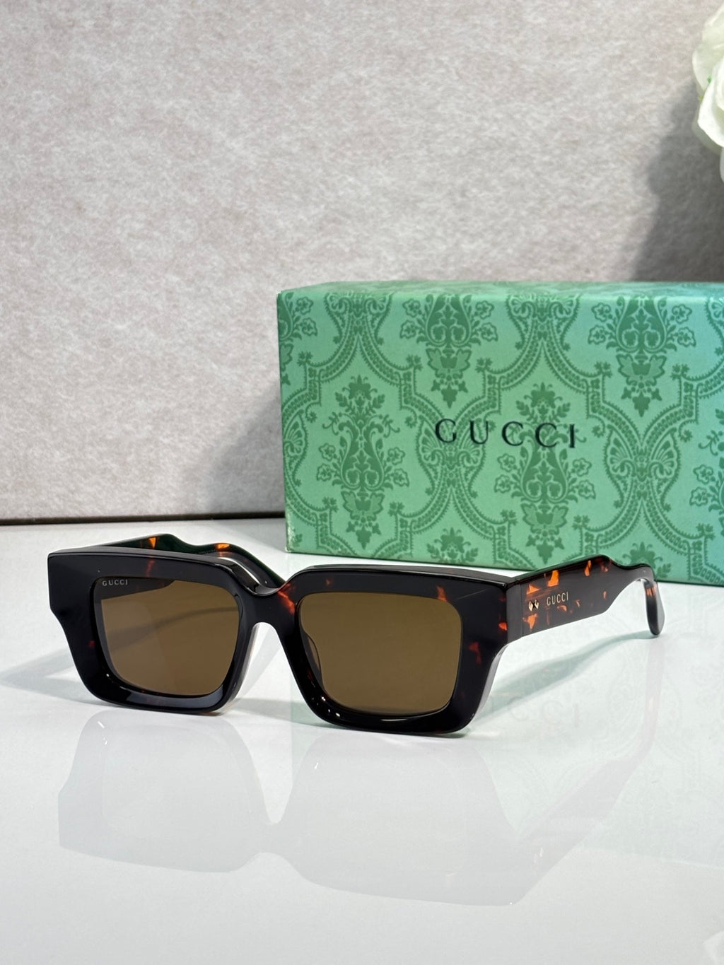 Black rectangular sunglasses with brown lenses and Gucci logo on side arms.