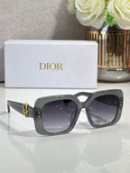 Dior sunglasses with charcoal gray frames and dark gradient lenses, gold hinge logo detail