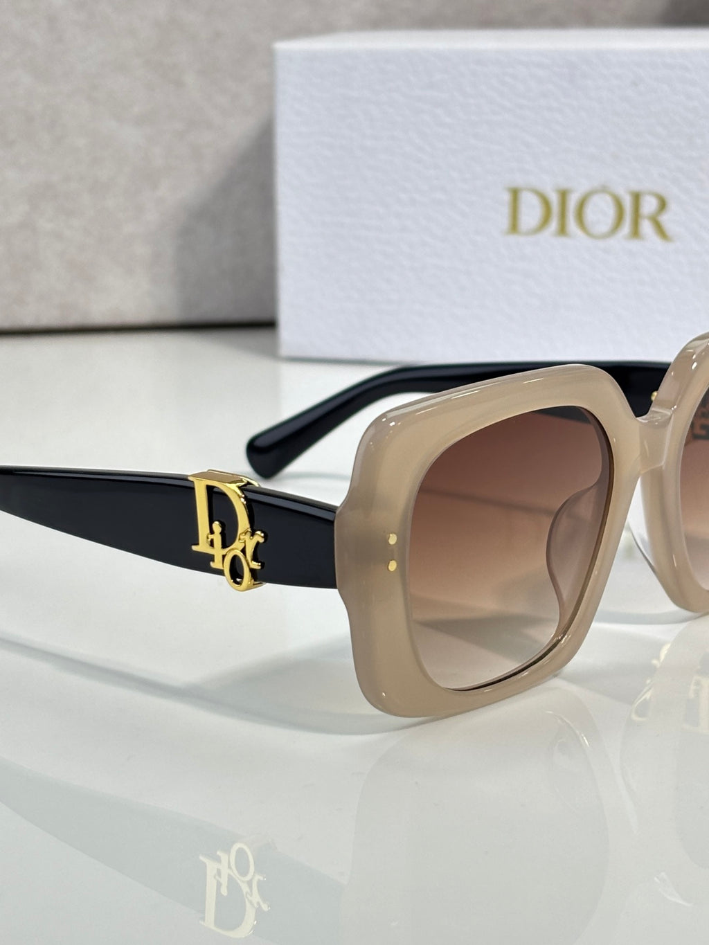 Dior sunglasses with beige and black frames, brown lenses, and gold side logo detail