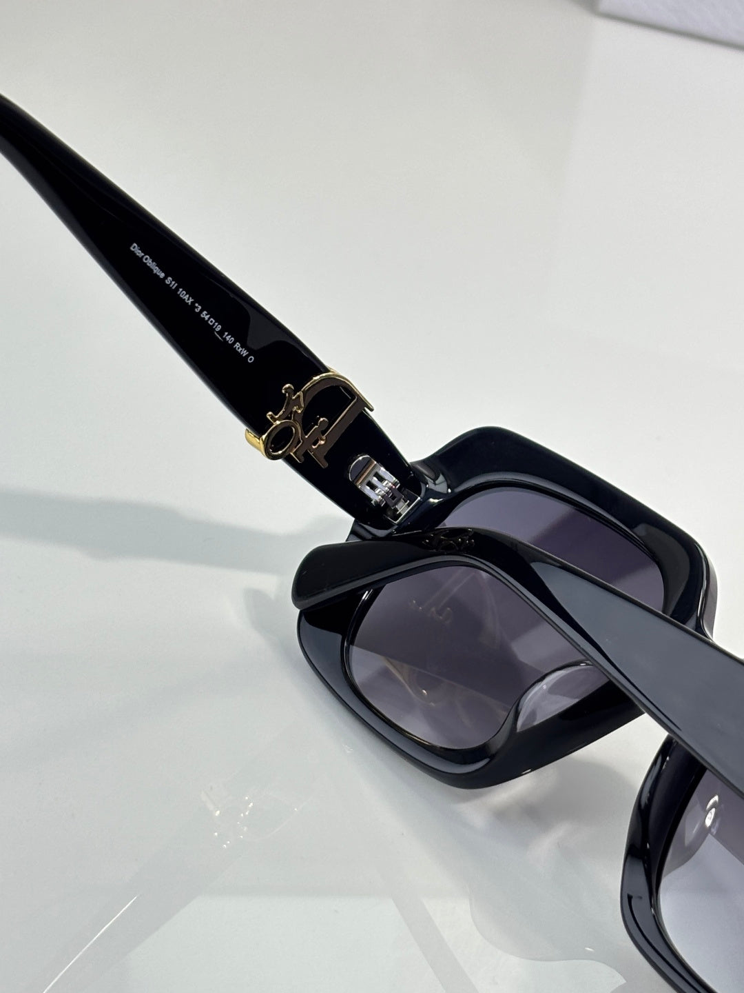 Black sunglasses arm and hinge with gold logo hardware and dark lens.