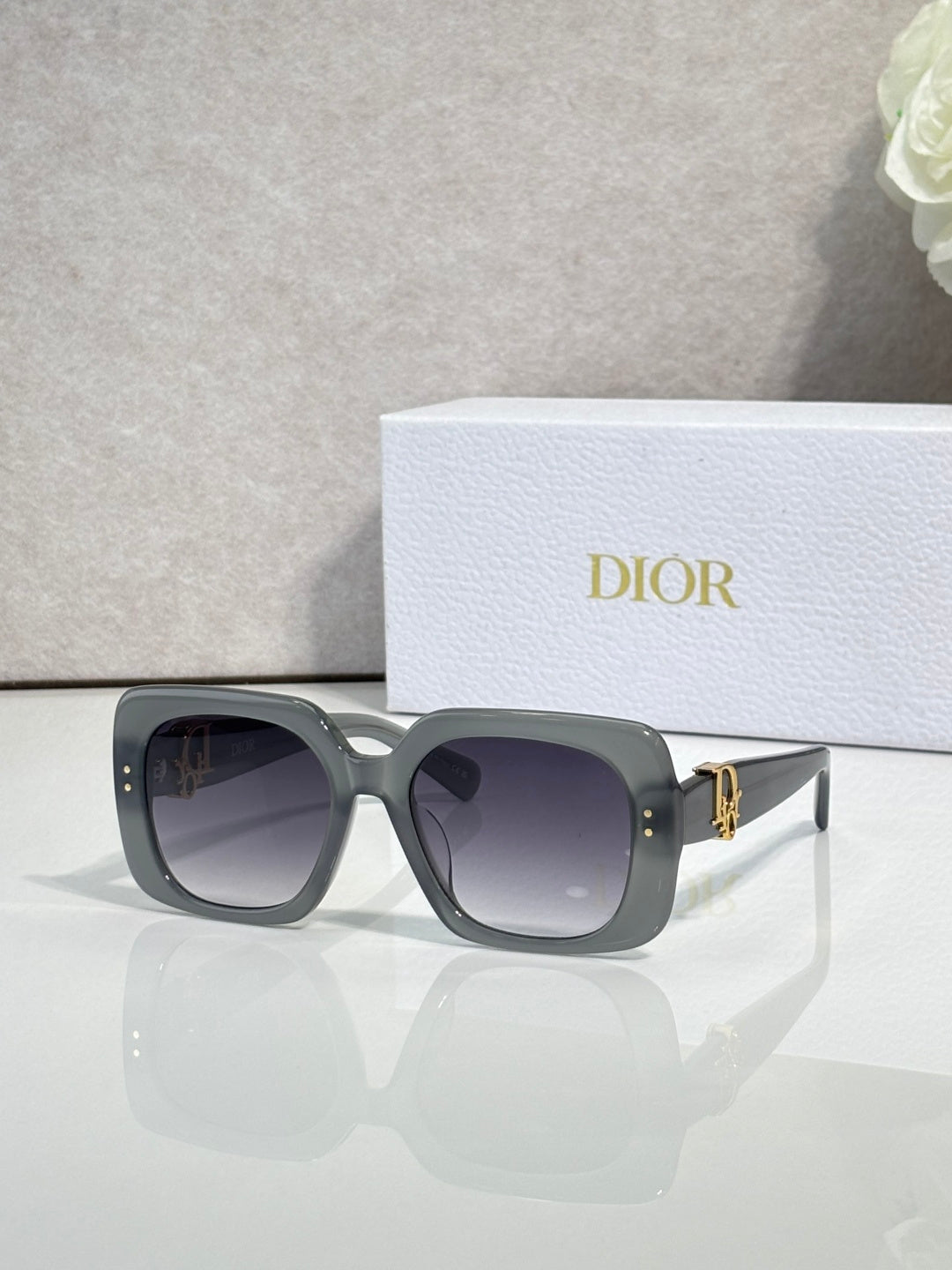 Dior sunglasses with dark gray frames and purple-gray gradient lenses, gold logo detail