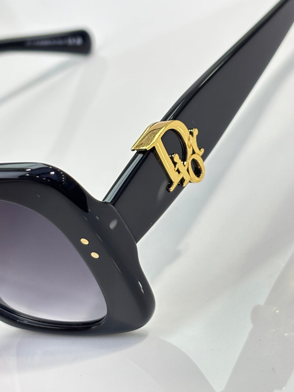 Black sunglasses arm with gold Dior logo detail and dark lens edge.