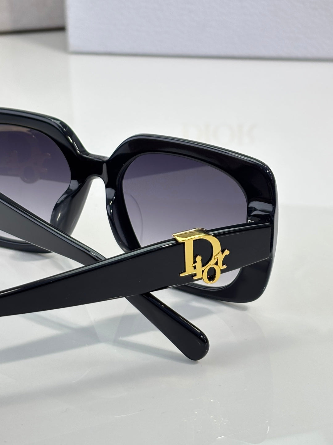 Black Dior sunglasses with gold D emblem on the temple and dark lenses.