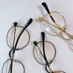 Round black eyeglasses with clear lenses and ornate gold-toned temple hardware