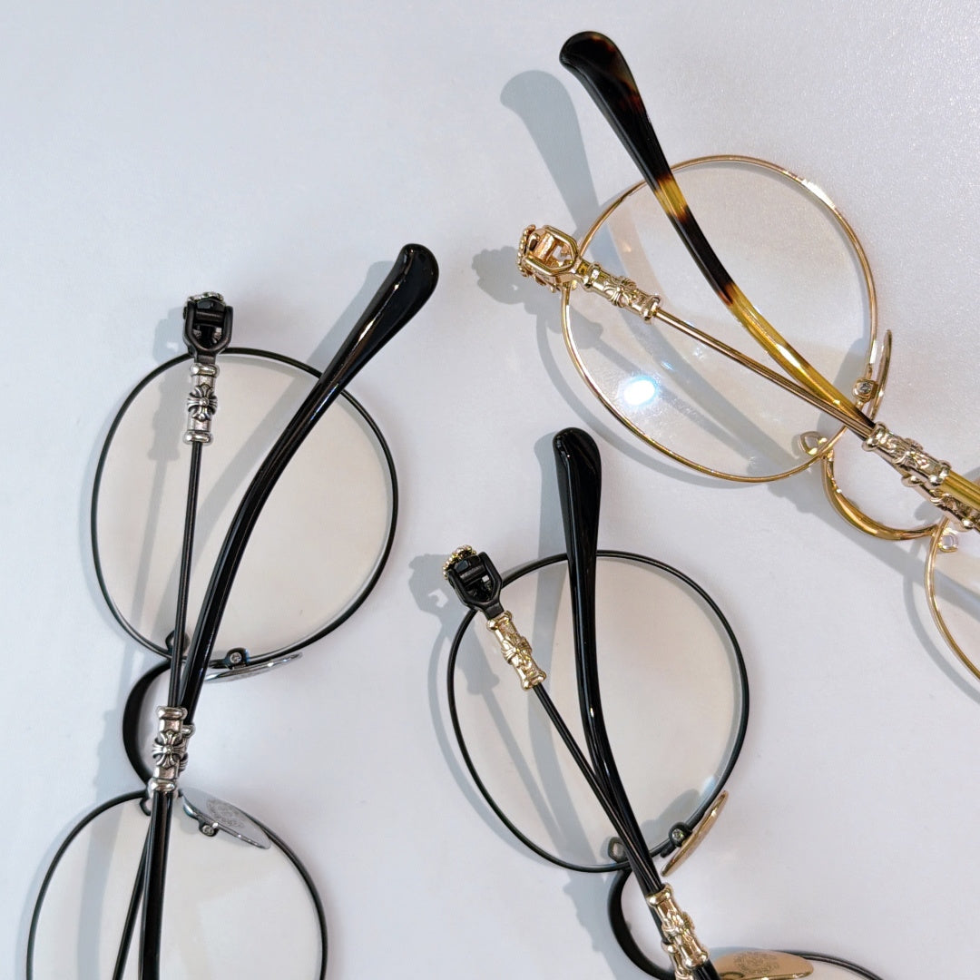 Round black eyeglasses with clear lenses and ornate gold-toned temple hardware