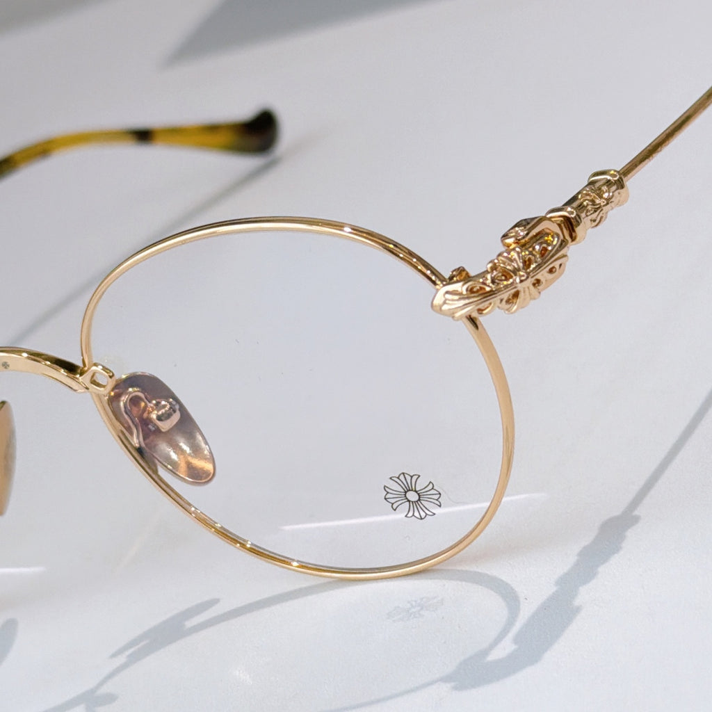 Round gold eyeglass frame with clear lenses and ornate gold temple detail