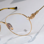 Round gold eyeglass frame with clear lenses and ornate gold temple detail