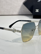 Close-up of square sunglasses with blue gradient lens and chain arm detail on metal frame.