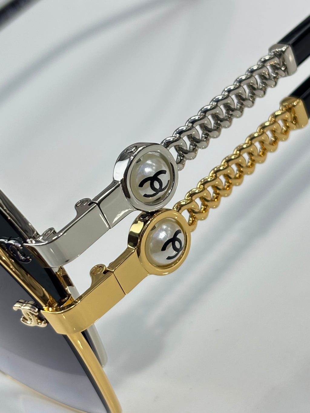 Close-up of metal chain bracelet-style detail and logo plaques on sunglasses frame arms.