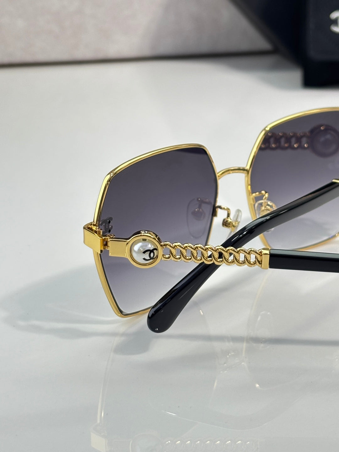 Chanel sunglasses angled view: gold square frame, dark gradient lenses, black temples
