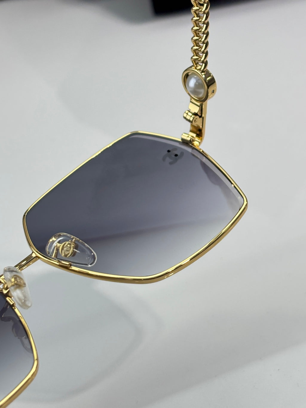 Chanel sunglasses close-up: gold lens and nose bridge with chain charm, dark tint