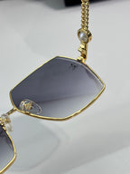 Chanel sunglasses close-up: gold lens and nose bridge with chain charm, dark tint