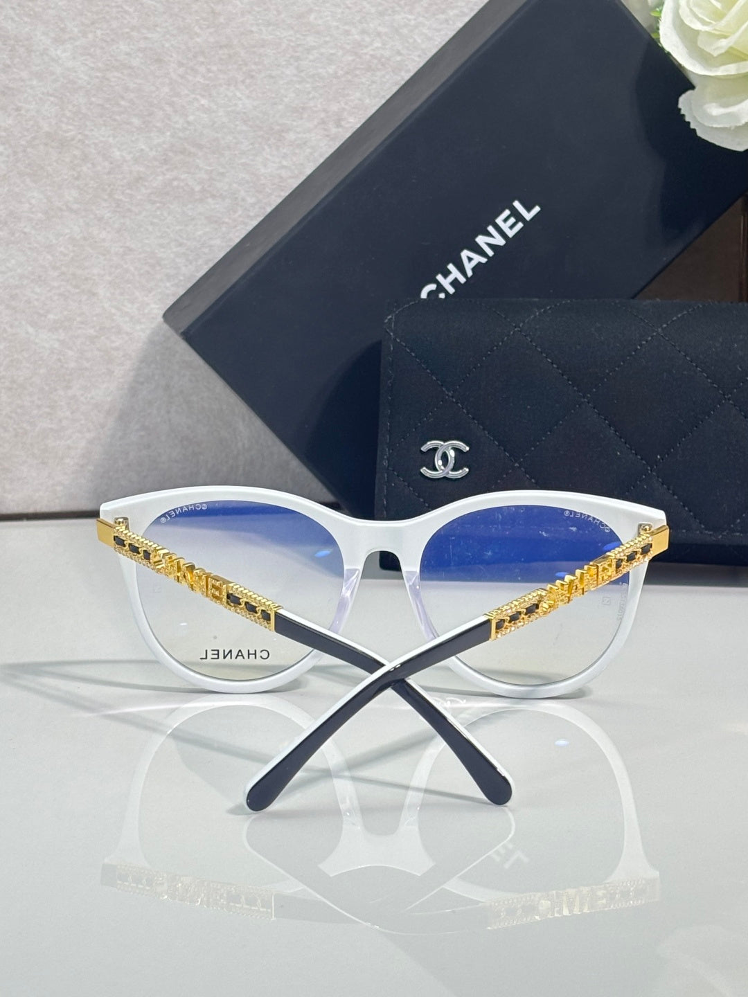 Chanel eyeglasses with white frames, blue lens fronts, and gold temple detail