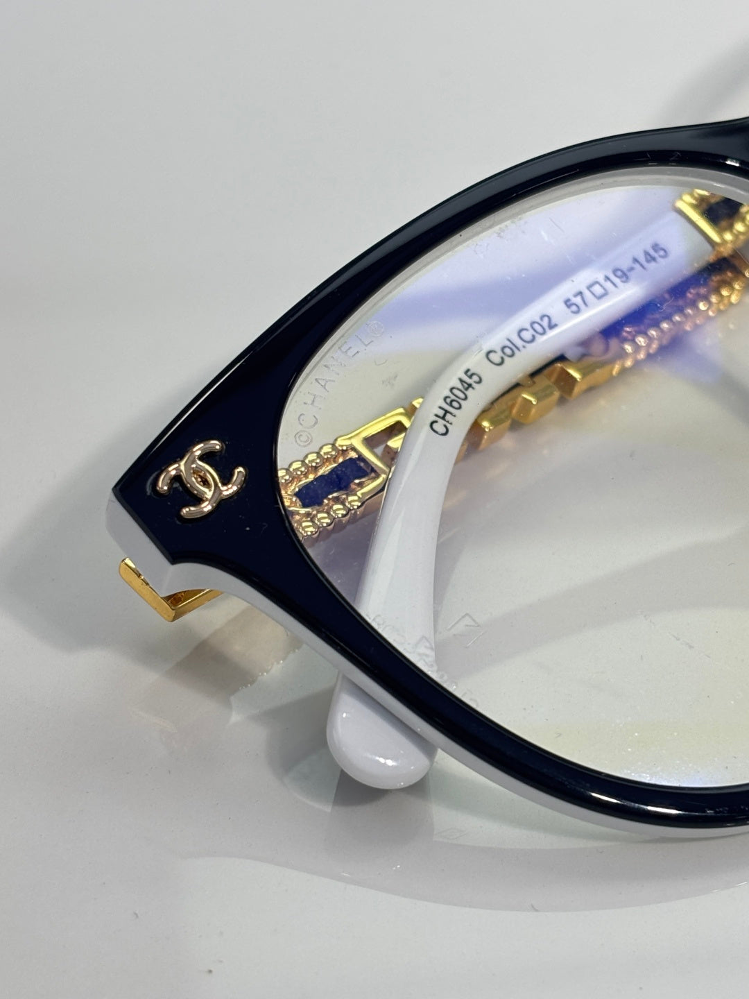 Chanel eyeglasses close-up: dark frame edge with gold logo and temple markings