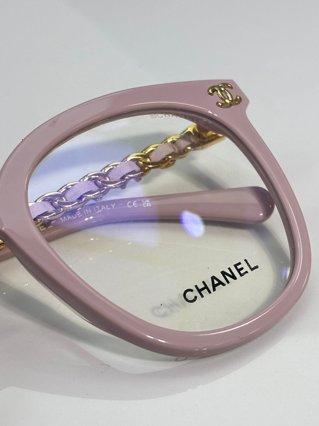 Light pink eyeglasses with engraved Chanel logo on the lens and gold chain detail