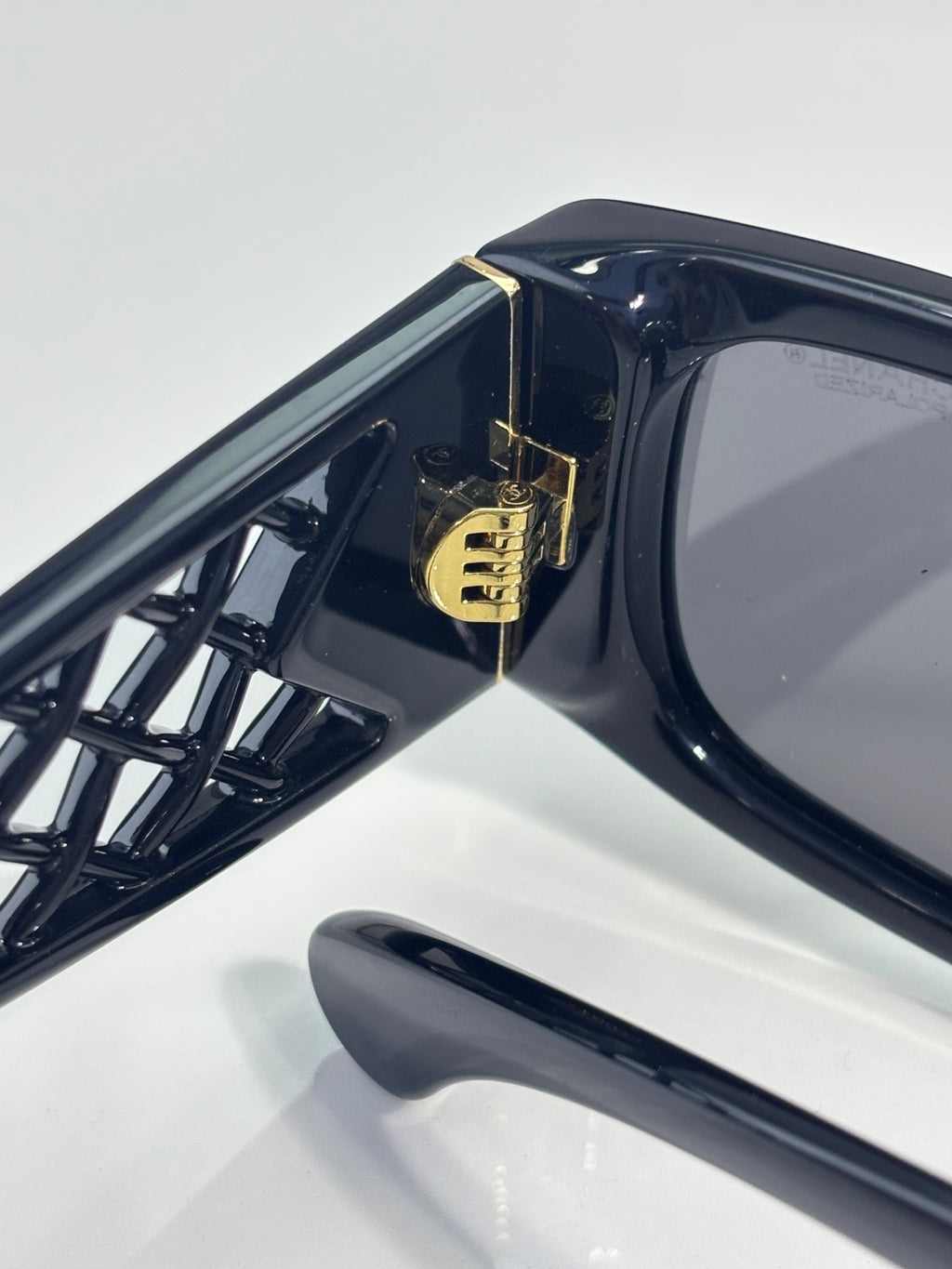 Black sunglasses temple close-up with gold CHANEL logo and glossy finish