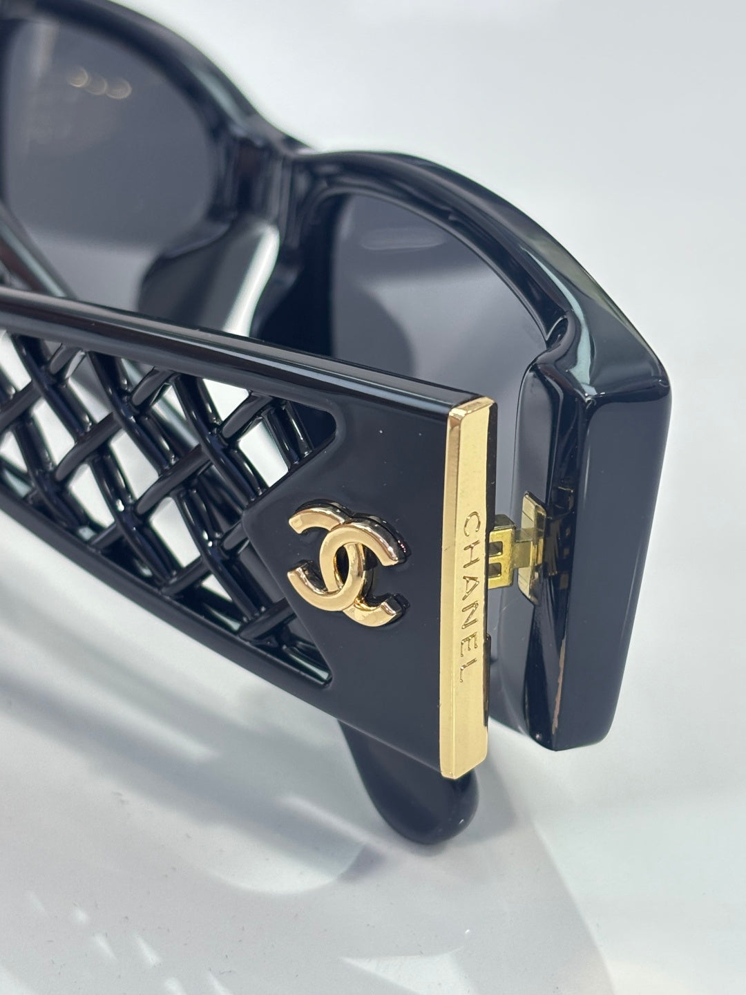Black sunglasses with gold logo plate and geometric lattice temple frame detail