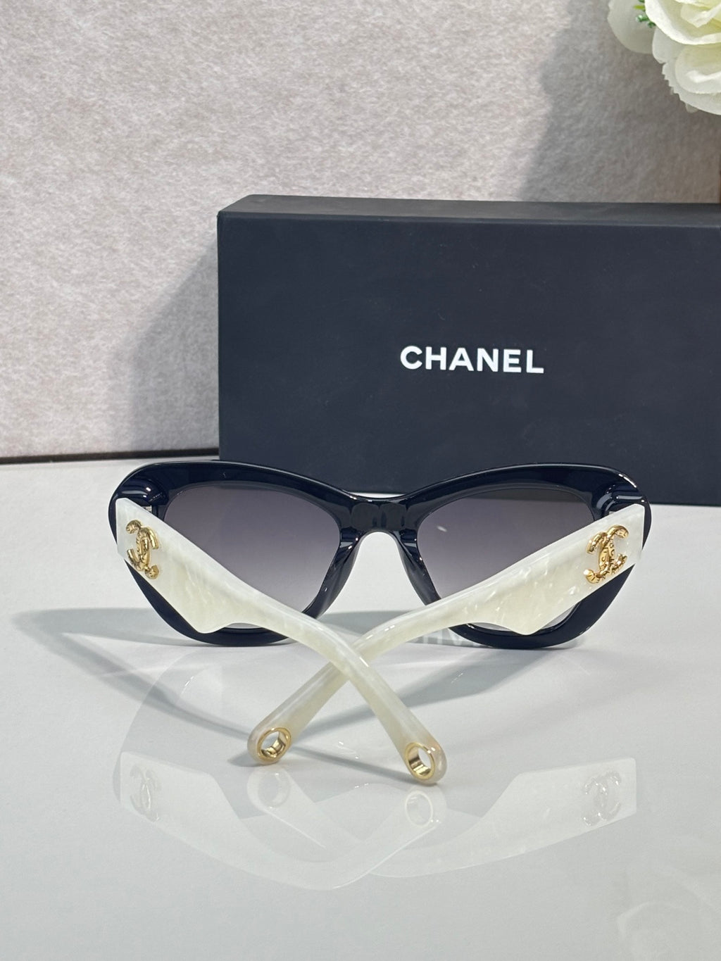 Chanel cat-eye sunglasses with black frames, clear arms, and gold logo emblems