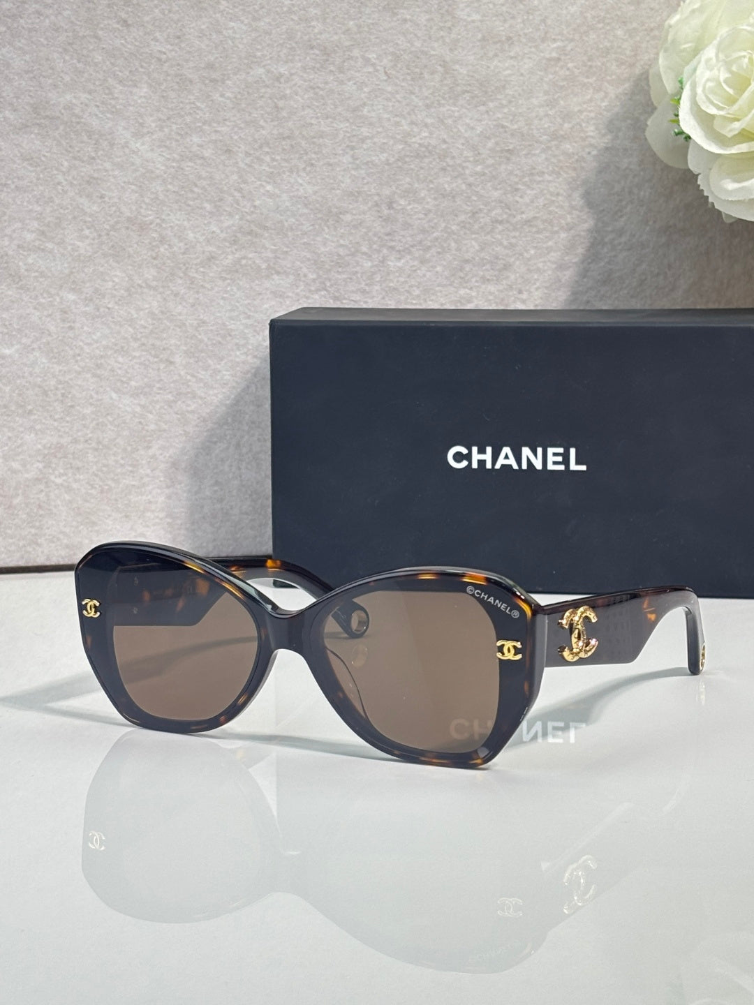 Dark sunglasses with gold emblem on temples, white accents, and tinted lenses