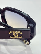 Dark sunglasses bridge close-up with gold logo detail and temple hinge