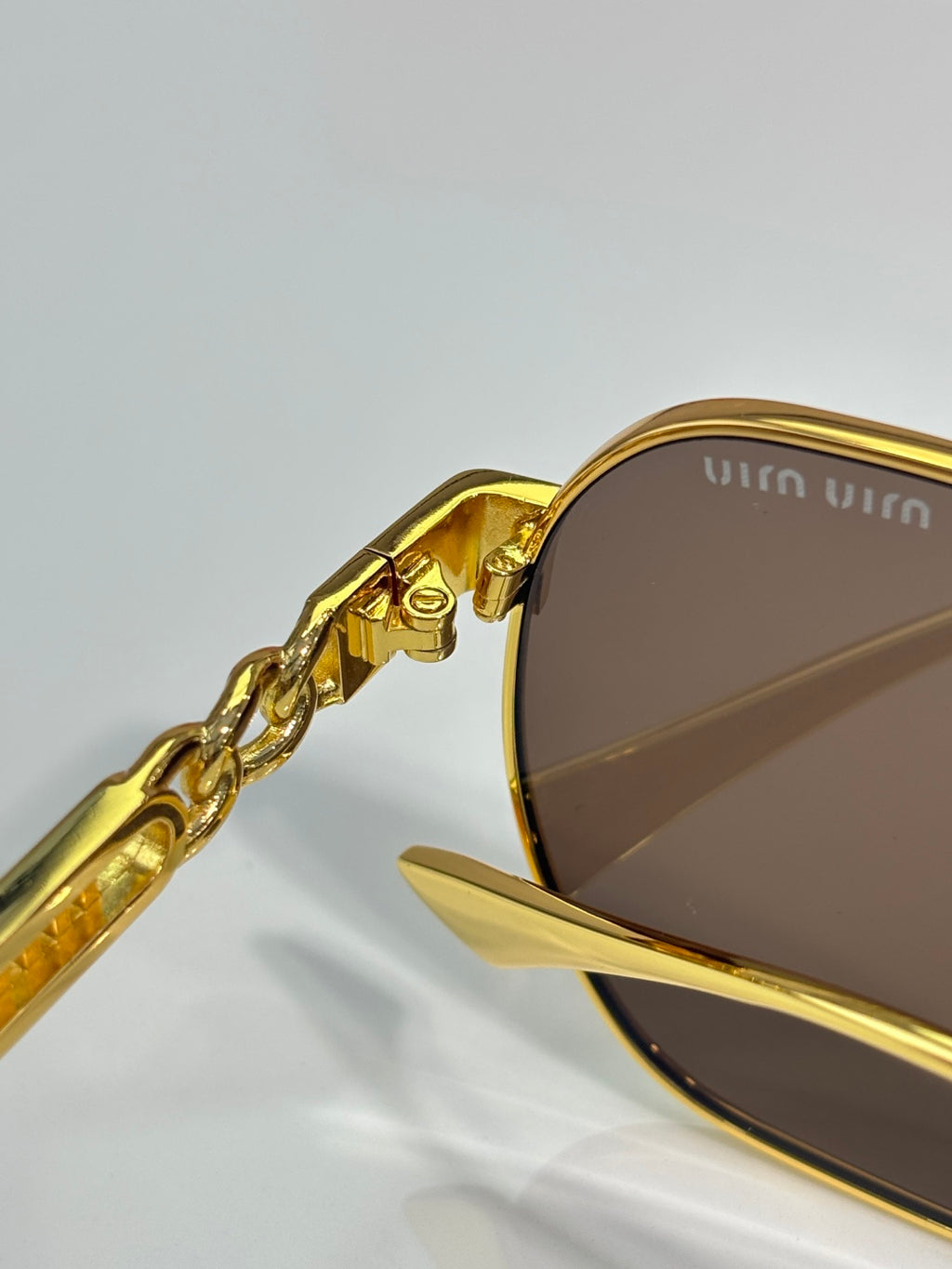 MiuMiu gold-tone sunglasses close-up with brown lens and temple hardware