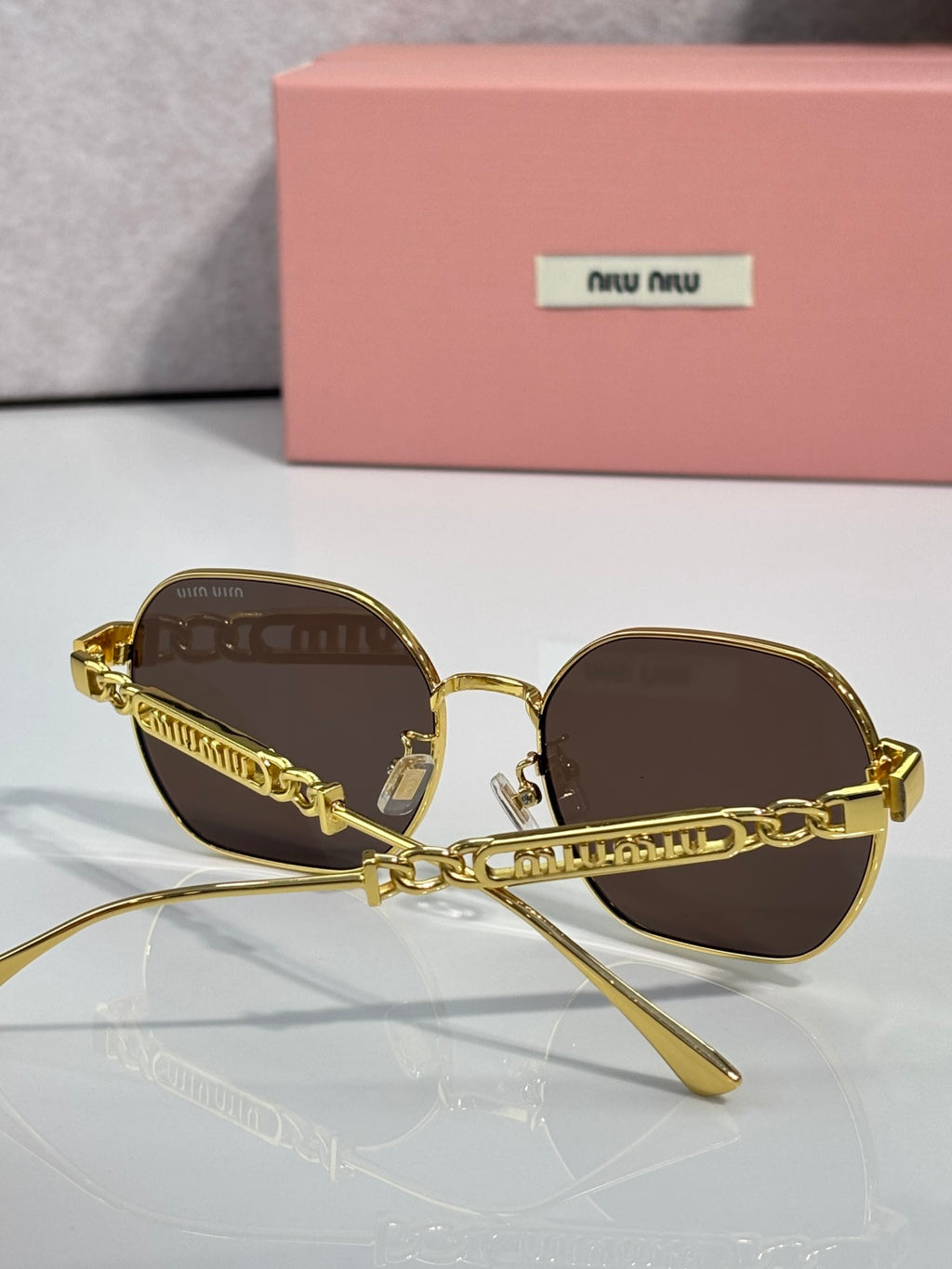 MiuMiu sunglasses with brown lenses, gold-tone frames, and chain link detail