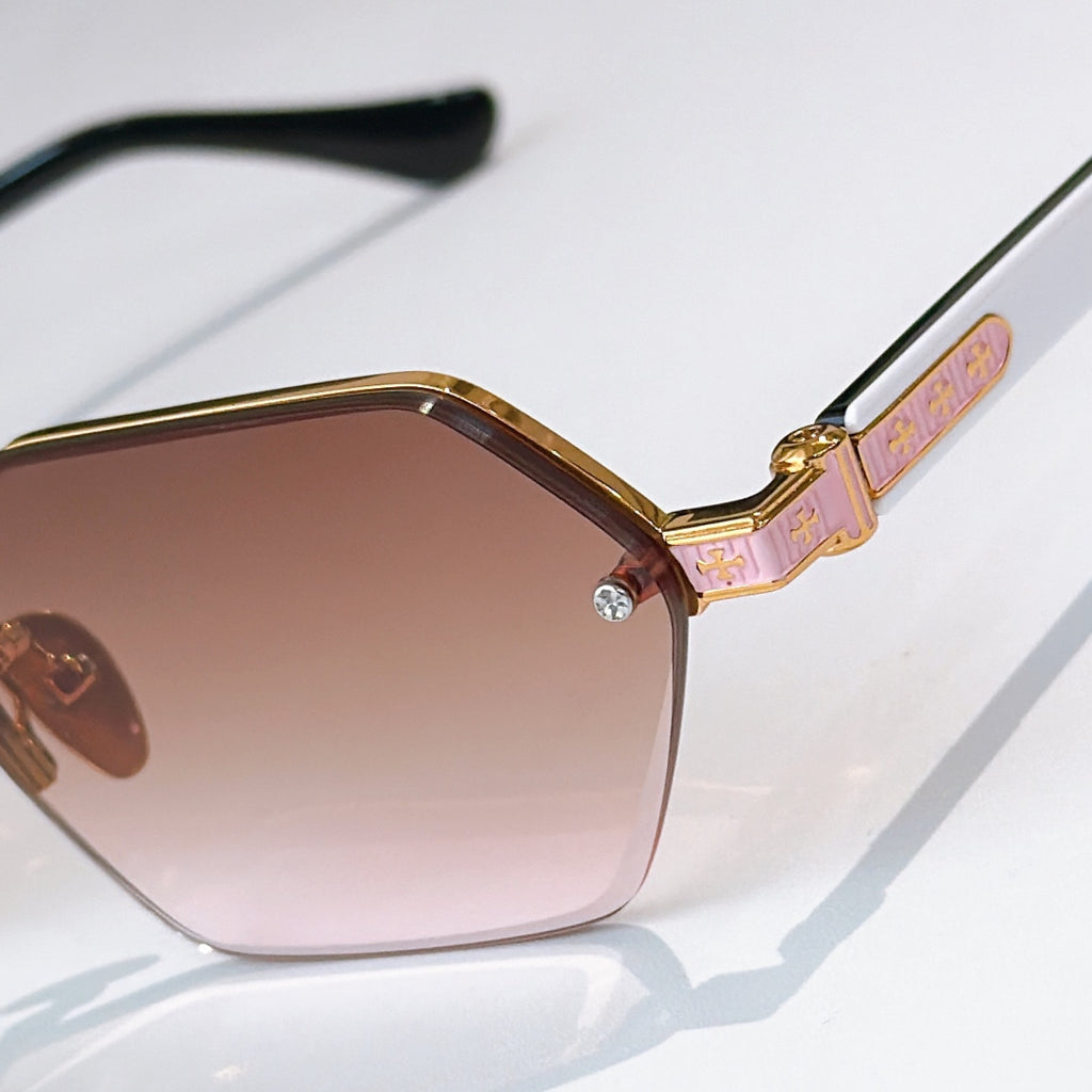 Gold sunglasses close-up: pink patterned temple and rose-tinted hexagonal lens