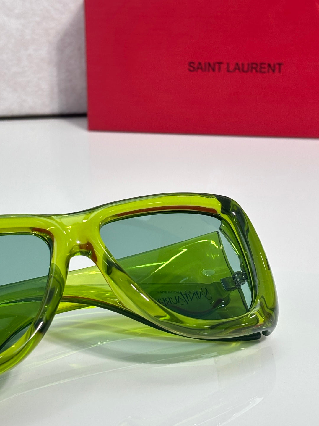 Green tinted sunglasses side view with curved clear frame, Saint Laurent