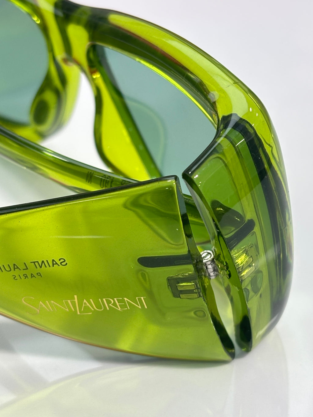 Green tinted sunglasses close-up, Saint Laurent branding on temple and lens