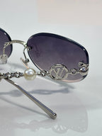 Louis Vuitton sunglasses close-up: dark lens, gold LV medallion bridge, chain detail