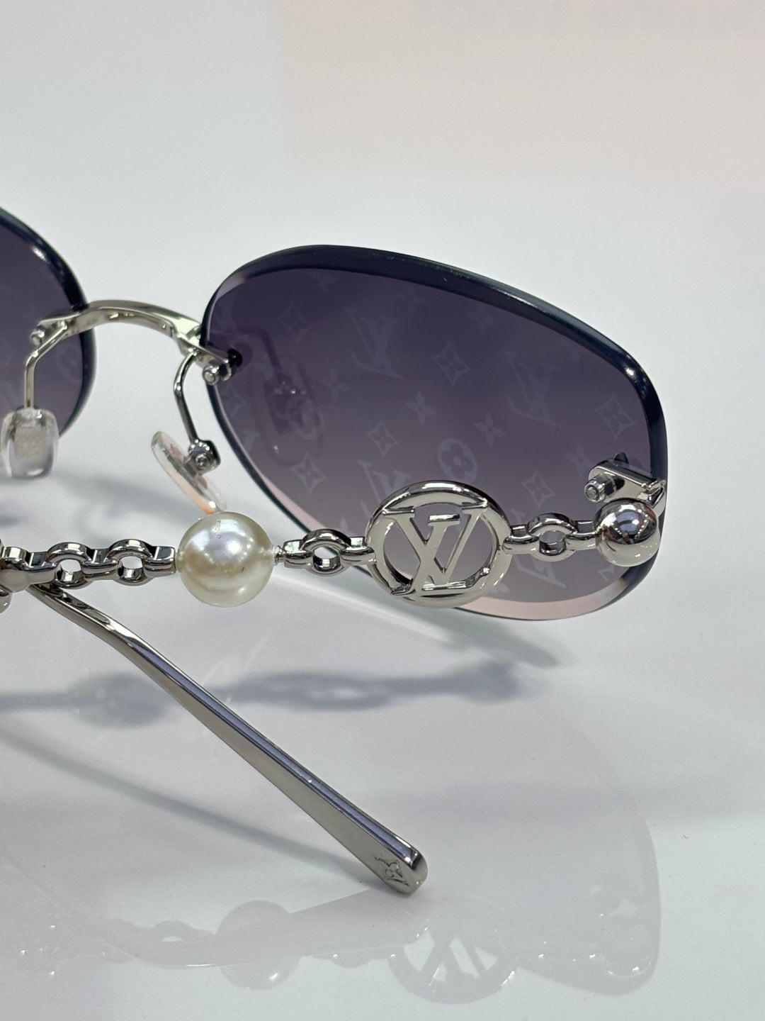 Louis Vuitton sunglasses close-up: dark lens, gold LV medallion bridge, chain detail