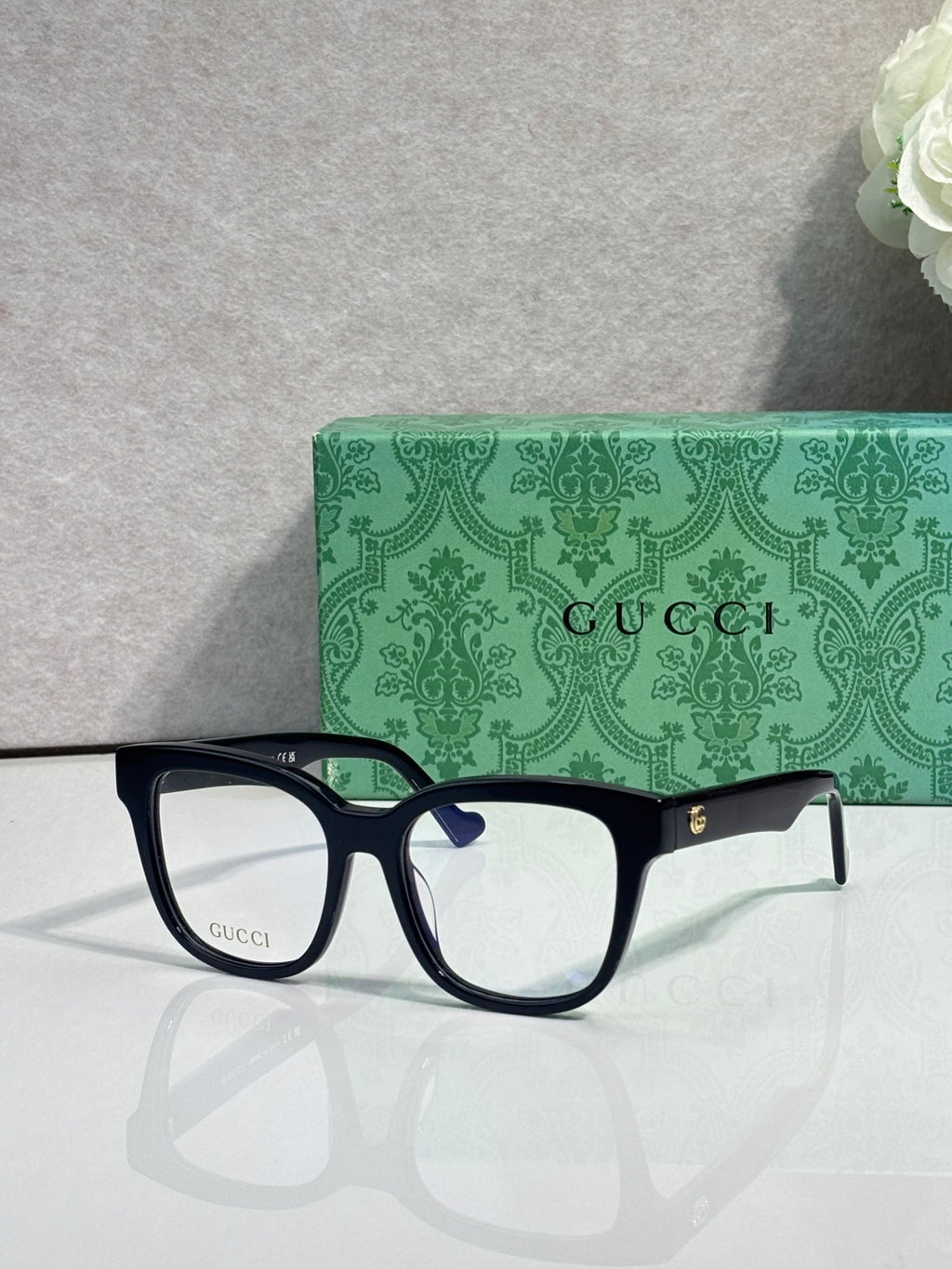 Rectangular eyeglasses with dark navy frame and gold temple logo, clear lenses