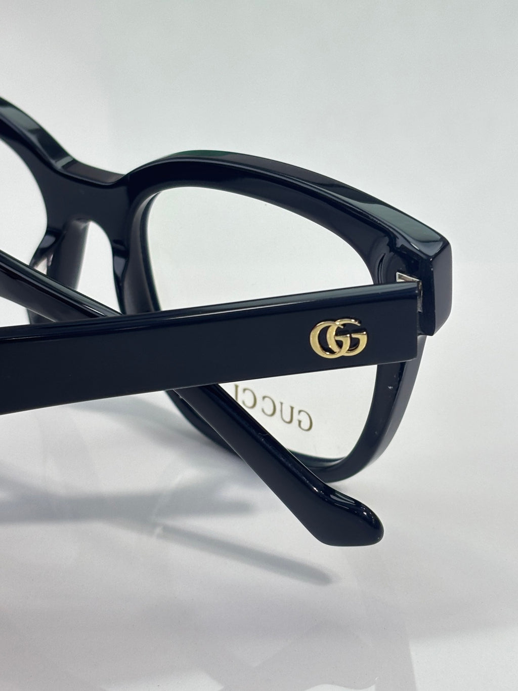 Eyeglass temple with gold double-G emblem on dark navy frame, clear lens visible