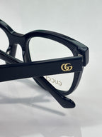 Eyeglass temple with gold double-G emblem on dark navy frame, clear lens visible