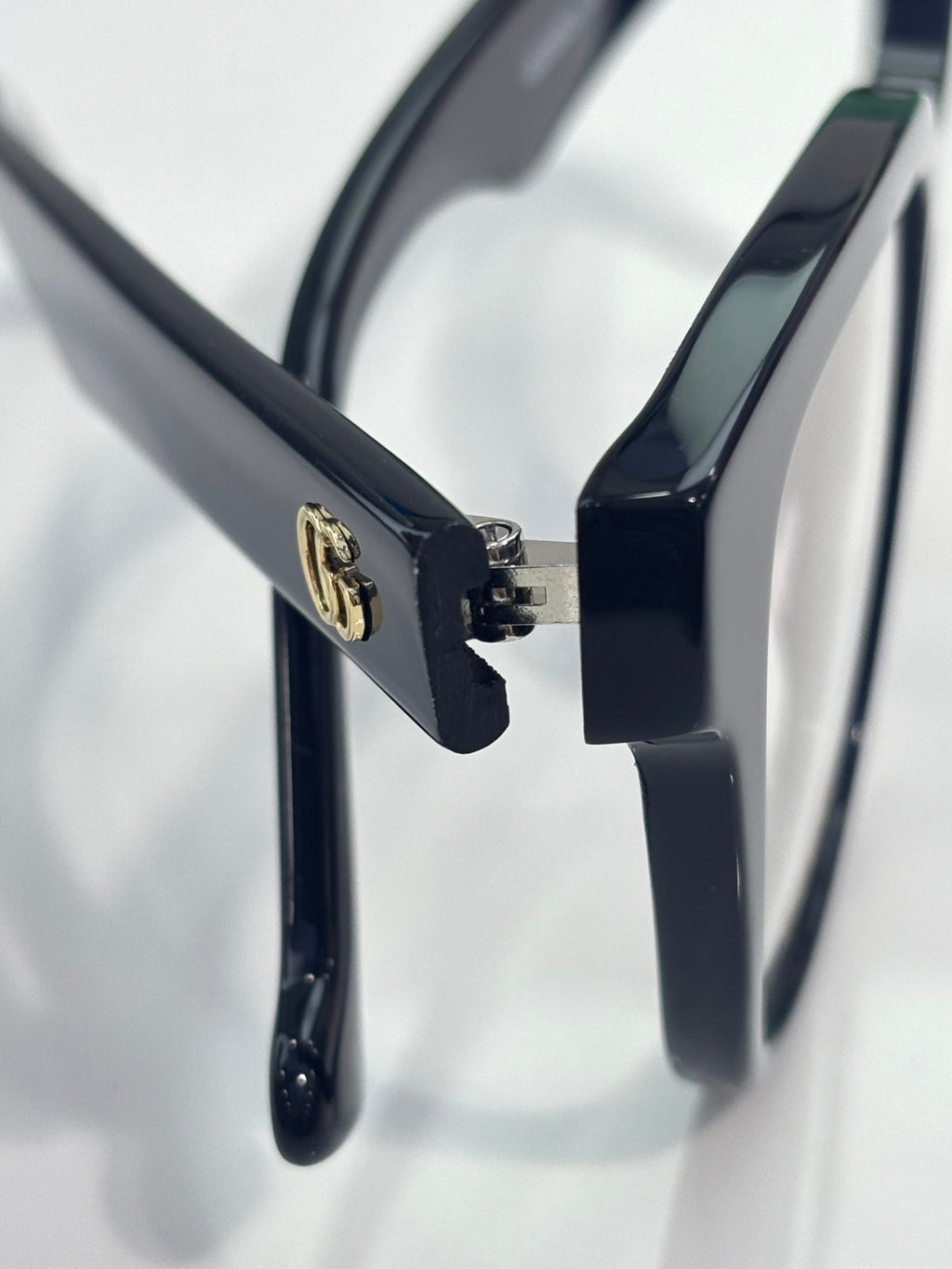 Eyeglass temple with gold logo detail on glossy dark navy frame, clear lens visible