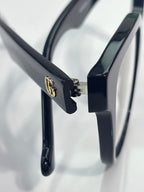 Eyeglass temple with gold logo detail on glossy dark navy frame, clear lens visible