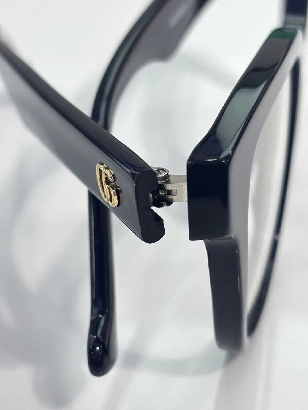 Eyeglass temple with gold logo detail on glossy dark navy frame, clear lens visible