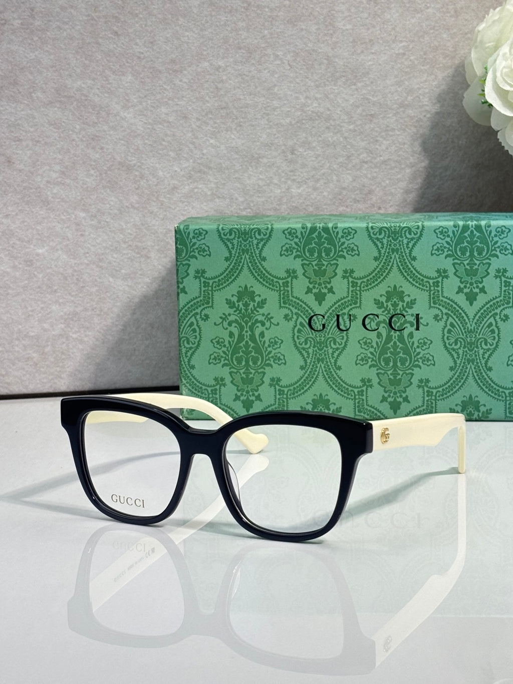 Rectangular eyeglasses with dark navy frame, gold G emblem at temple, clear lenses
