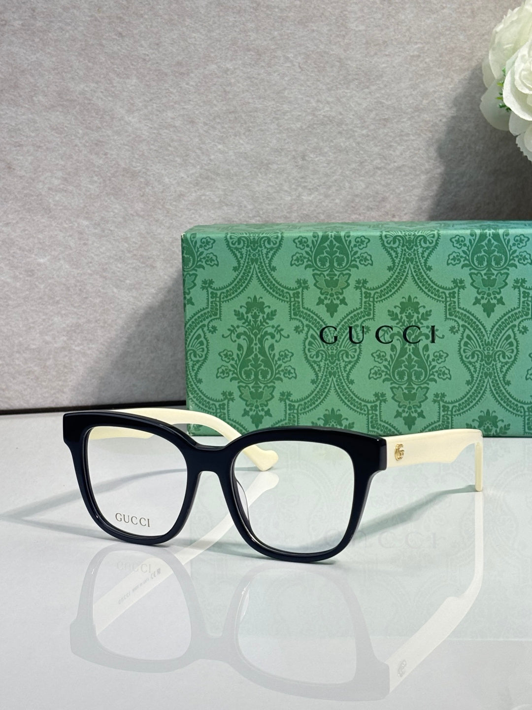 Rectangular eyeglasses with dark navy frame, gold G emblem at temple, clear lenses
