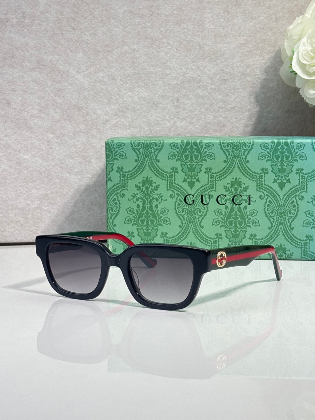 Gucci sunglasses, black frame with red-green temple accents, dark tinted lenses