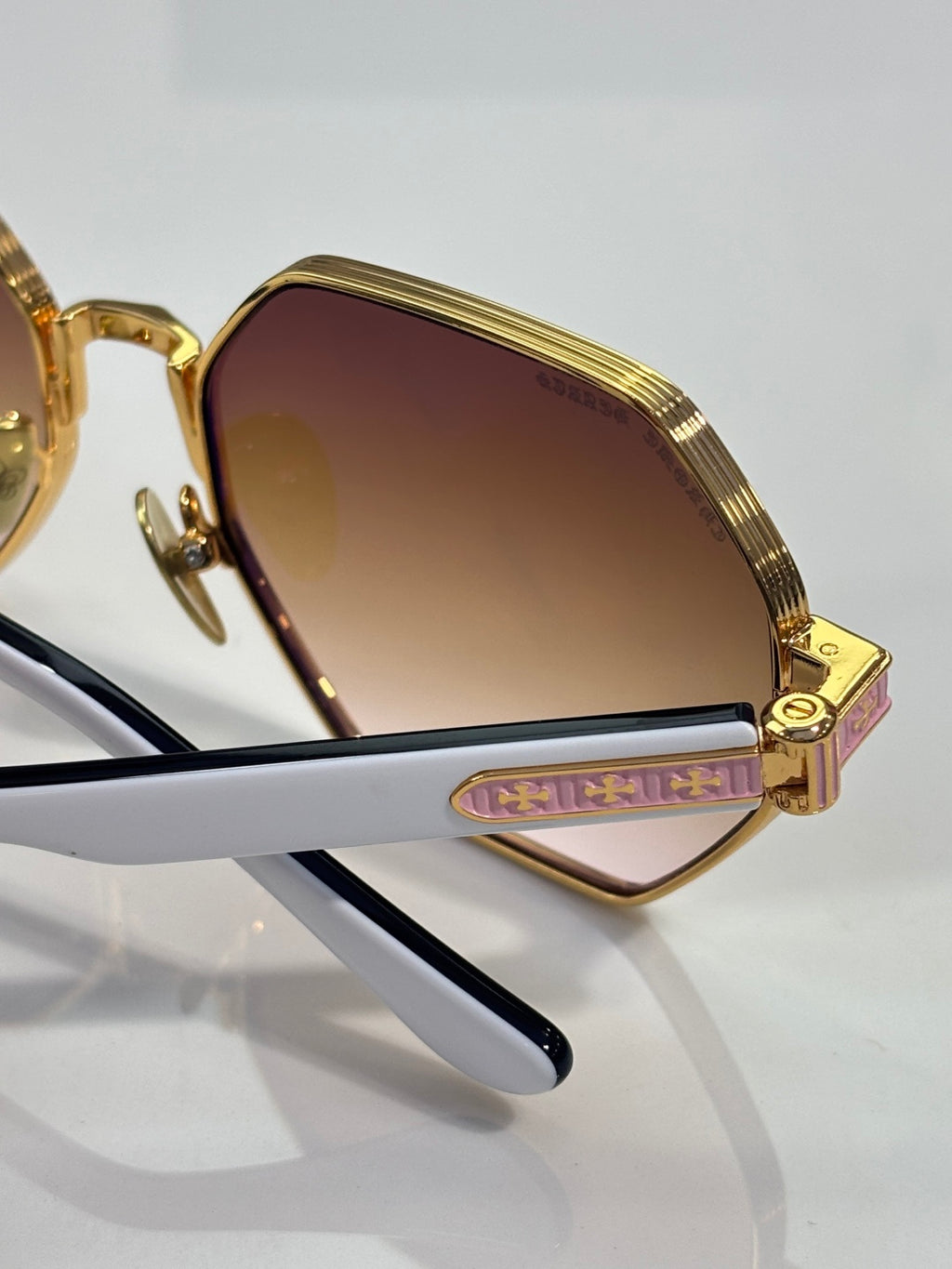 Chrome sunglasses close-up: gold frame, gradient lens, and side logo detail