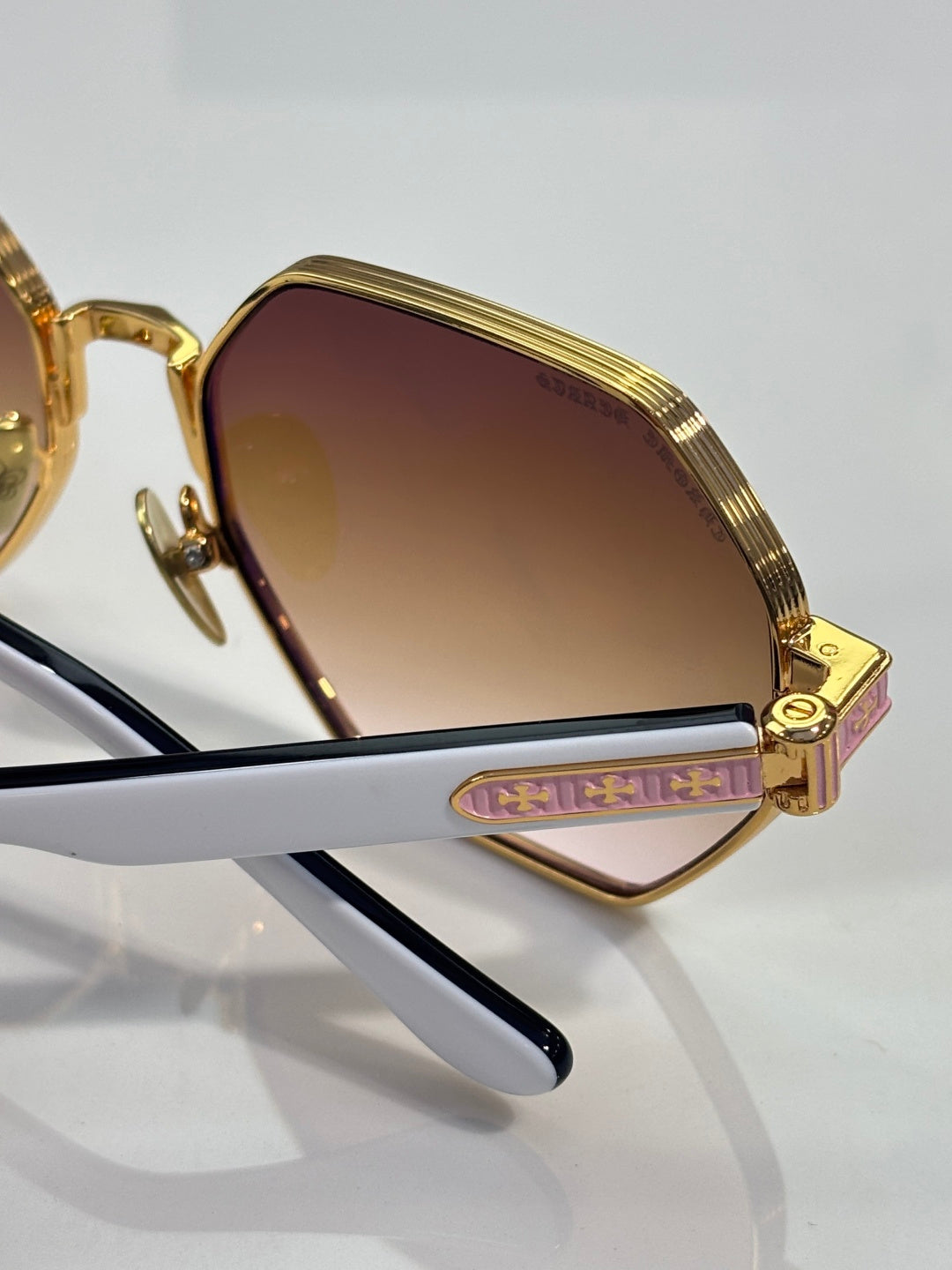 Chrome sunglasses close-up: gold frame, gradient lens, and side logo detail