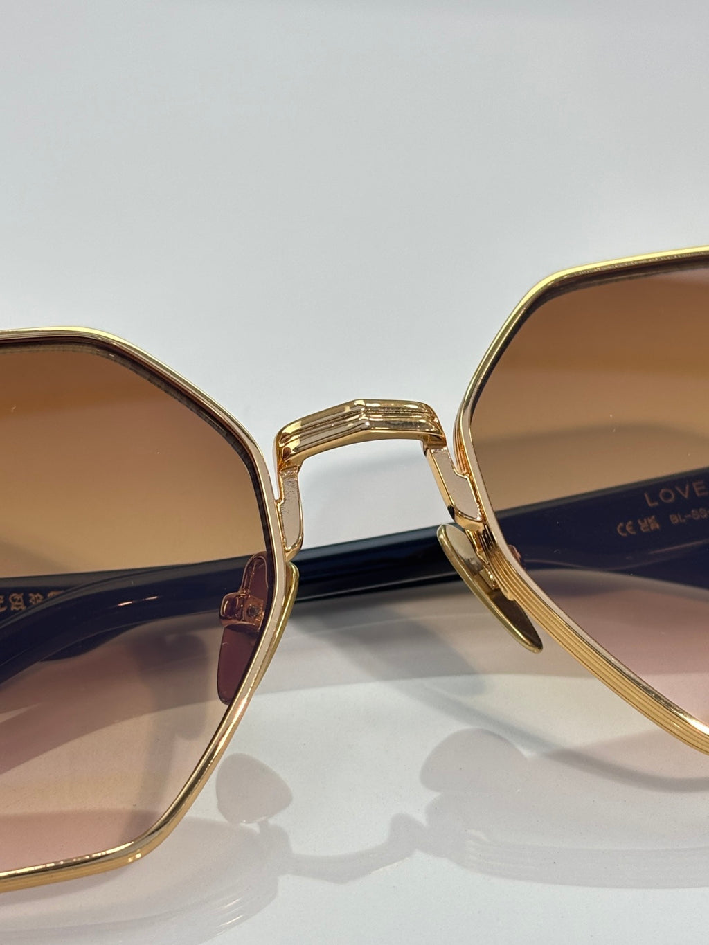 Chrome sunglasses close-up: gold frame with warm gradient lens and side arm text