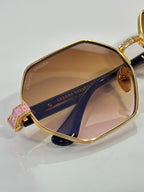 Chrome sunglasses close-up: gold frame with amber lenses and engraved side panel