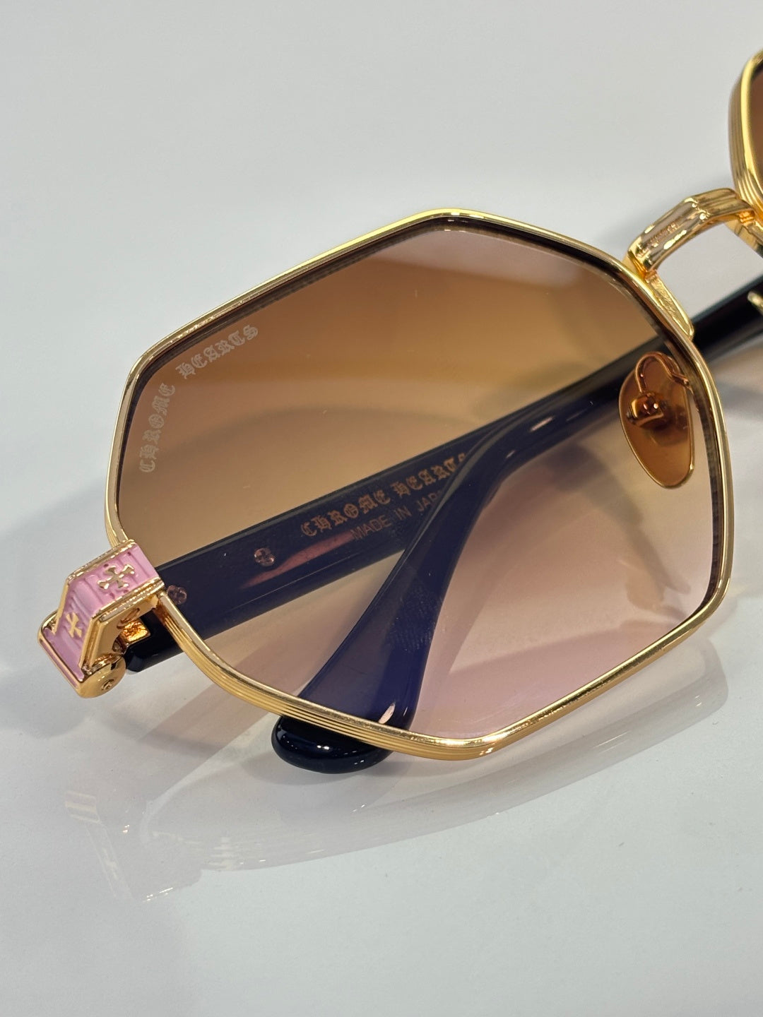 Chrome sunglasses close-up: gold frame with amber lenses and engraved side panel