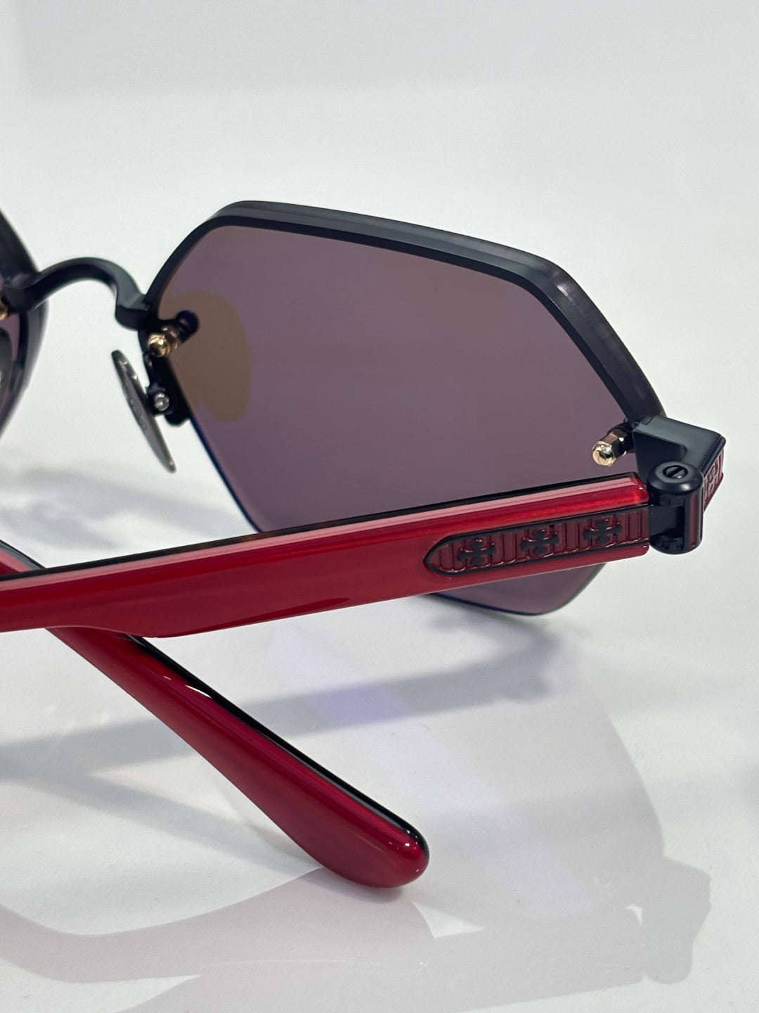 Close-up of hexagon sunglasses with purple-tinted lens and red temple arm